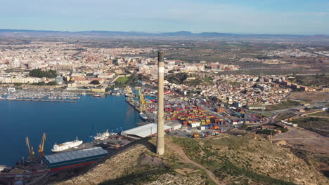 Toma-Aérea-De-Chimenea-Cartagena-España-Día-Soleado-Zona-Industrial-Mar-Mediterráneo